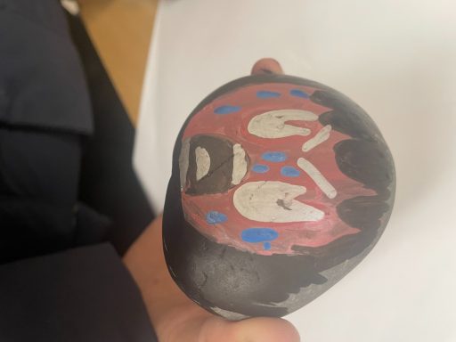 Hand-painted wooden figure with red and blue facial designs and exaggerated features.